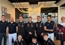 ASC Grünwettersbach startet Medical Partnerschaft mit dem Gelenkquartier für Bundesliga Tischtennis Eleven teammates in black jackets pose for a team photo in a modern office, with one holding a red-and-black jersey.